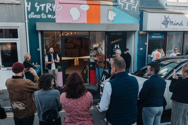 A crowd gathers in the street for the opening of Y Stryd, a cafe with a colourful mural, next door to Llanelli Mind