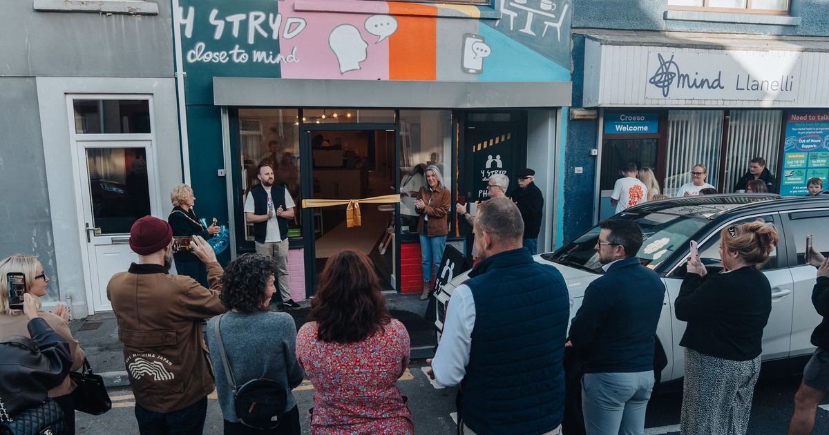 A crowd gathers in the street for the opening of Y Stryd, a cafe with a colourful mural, next door to Llanelli Mind