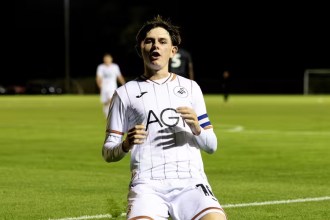 Swansea City Under-21s captain Yori Griffith, wearing the armband, slides on his knees in celebration under the floodlights.