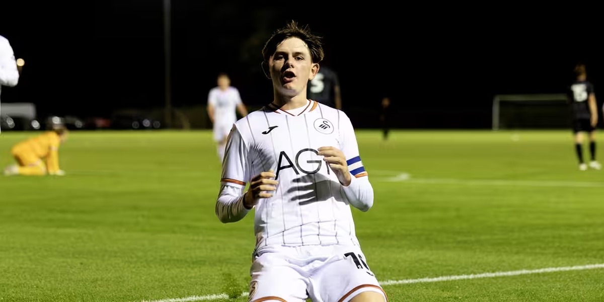 Swansea City Under-21s captain Yori Griffith, wearing the armband, slides on his knees in celebration under the floodlights.