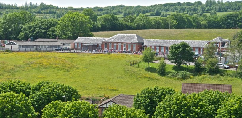 Ysgol Llandybie primary school, a long red-brick building with a grass field in front and wooded hills behind