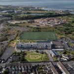 Aerial view of Ysgol Pen Rhos primary school in Llanelli and its green 3G pitch, with the AMG Resources waste site and the Loughor estuary beyond