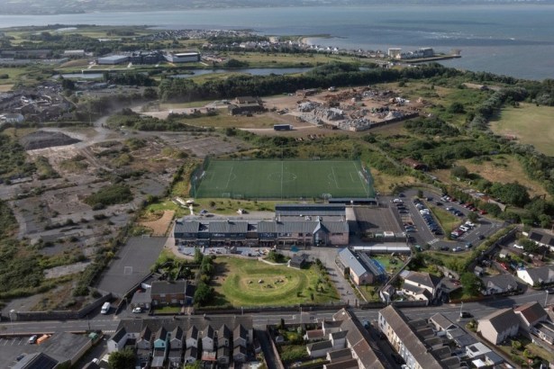 Aerial view of Ysgol Pen Rhos primary school in Llanelli and its green 3G pitch, with the AMG Resources waste site and the Loughor estuary beyond